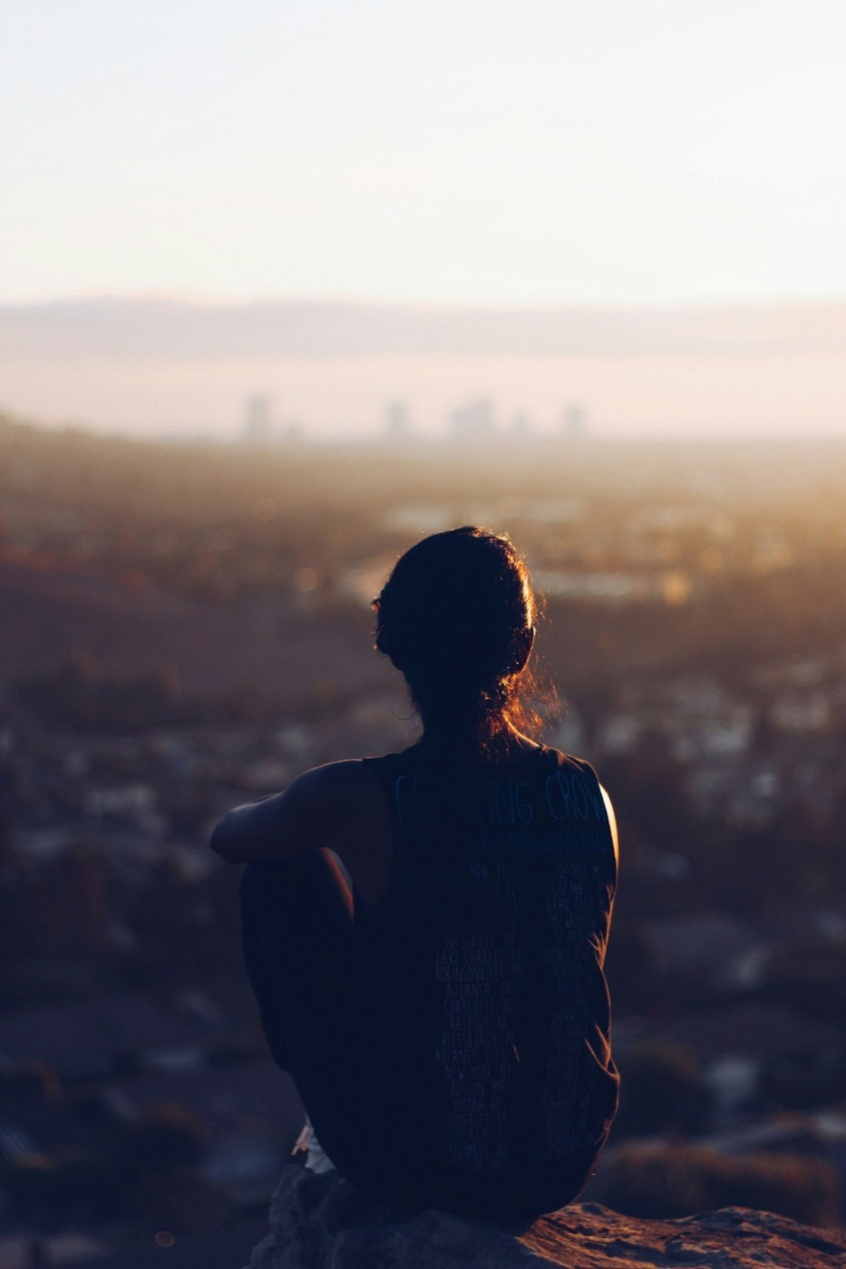 A person sitting on a hillside at dusk, looking out over a city